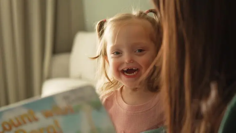 A young girl smiles while someone reads her a picture book