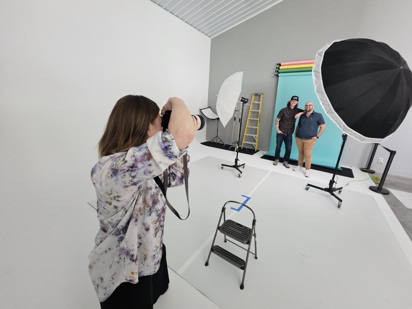A photographer capturing two smiling men posing against a colorful backdrop in a well-lit photo studio.