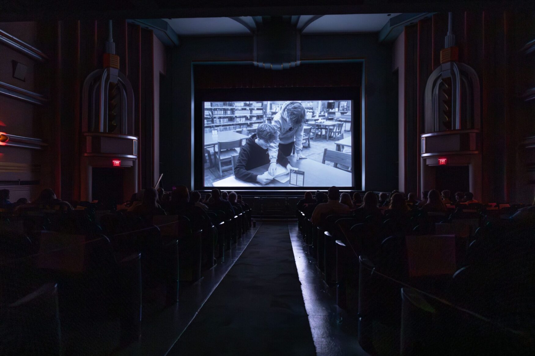 Interior of a theater during a film festival showing a black and white movie, with attendees watching intently in the dimly lit hall.