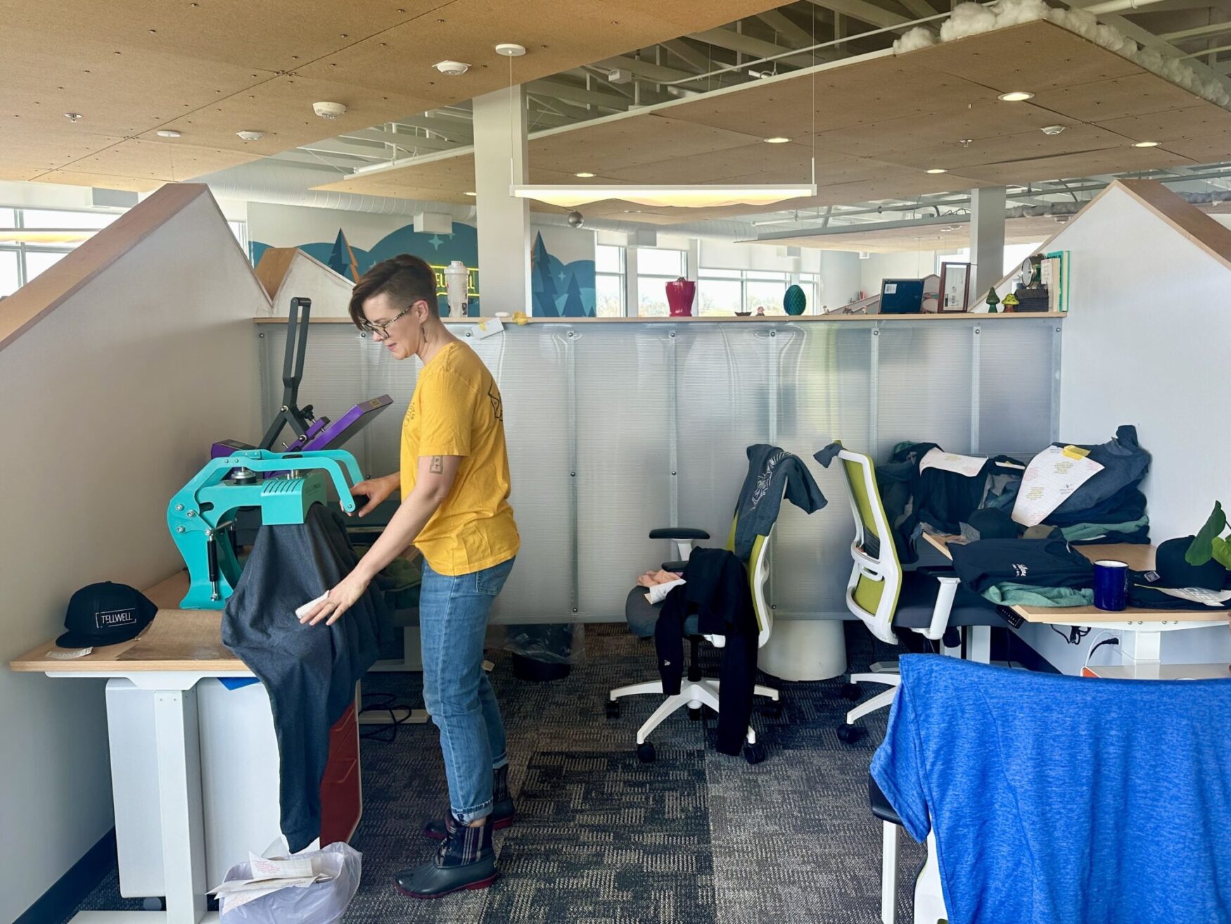 A person operating a heat press machine, carefully aligning a garment to apply a design, in an office space.