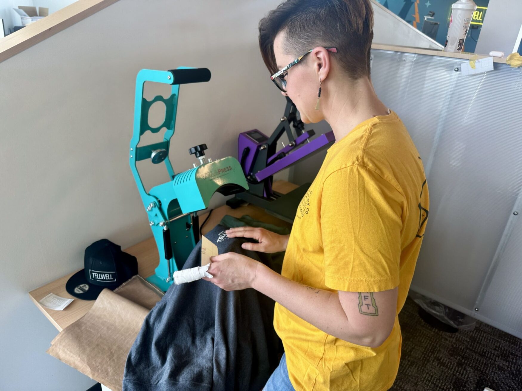 Close-up of a person pressing a decal onto a t-shirt with a heat press machine in a bright, modern office.