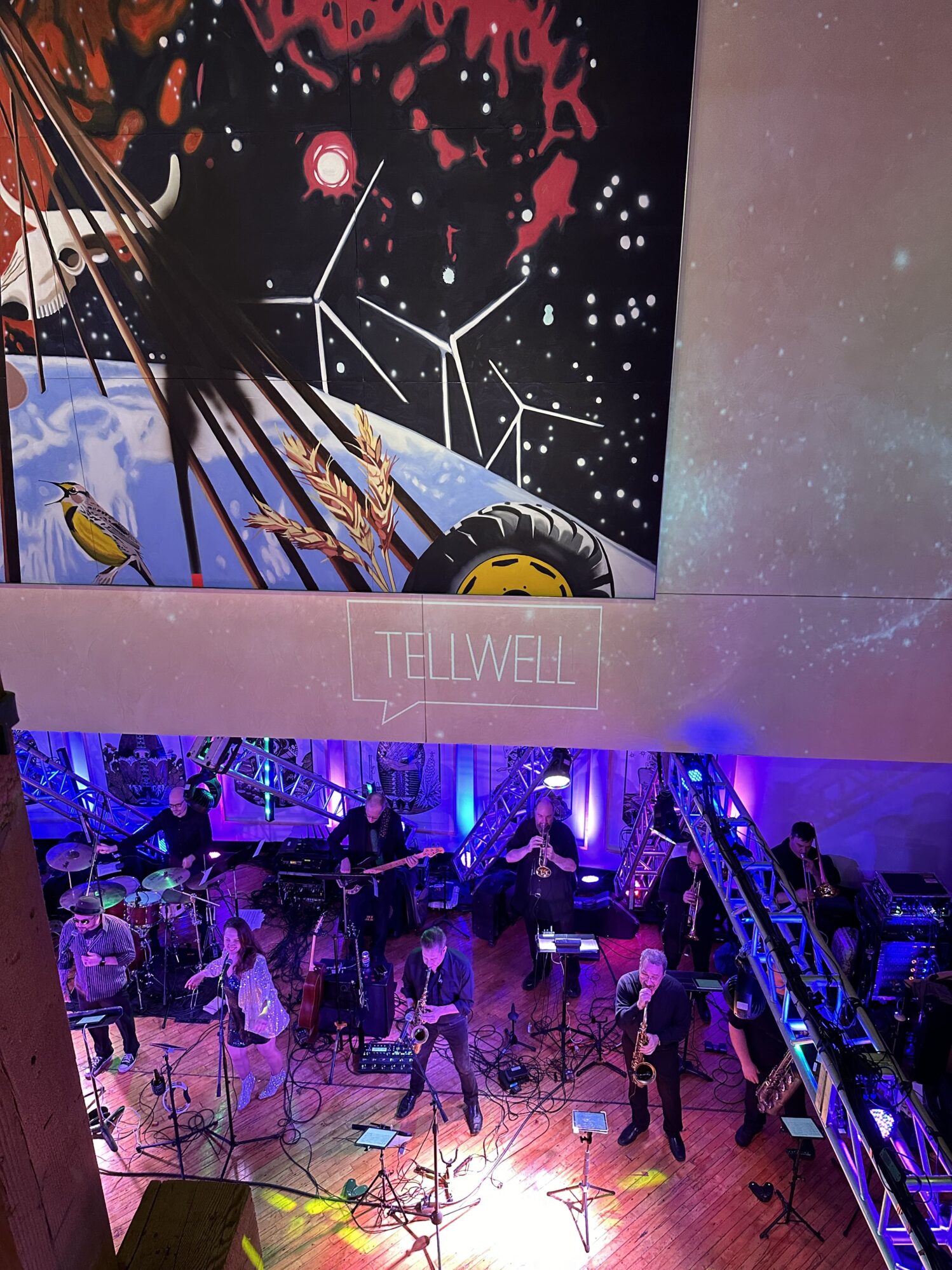 An aerial view of a live band performance in a large hall, showing multiple musicians playing instruments with intricate stage lighting, creating a dynamic and vibrant music event.