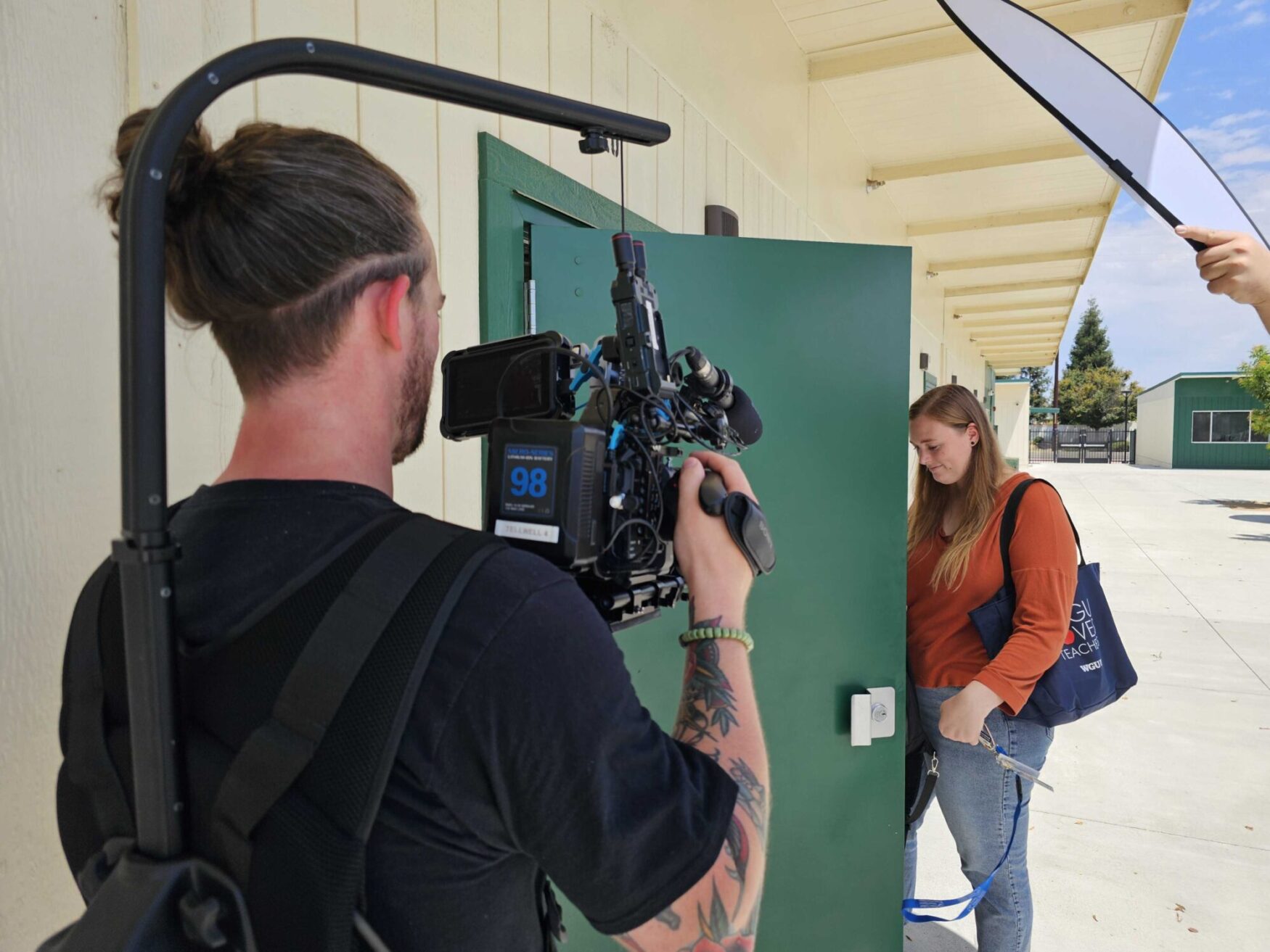 Duncan filming a woman entering a building. It's sunny.
