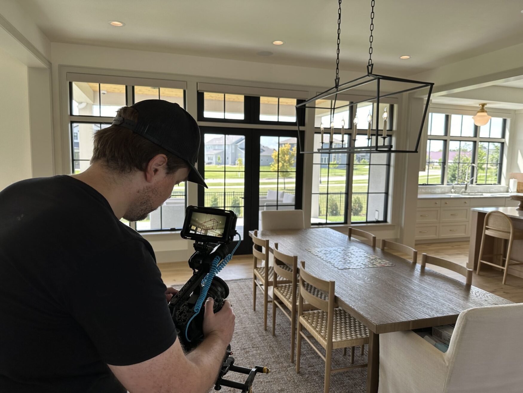 Matt films a room. There is a light colored table surrounded by wooden chairs. The room is clean and styled.