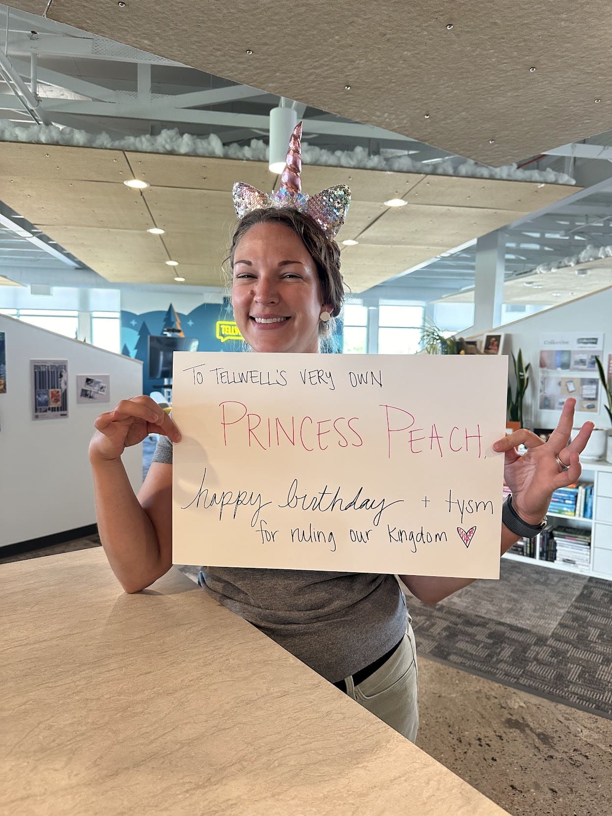 Annie holds a sign that says "To Tellwell's very own Princess Peach, happy birthday and tysm for ruling our kingdom." She's wearing a unicorn headband and smiling.