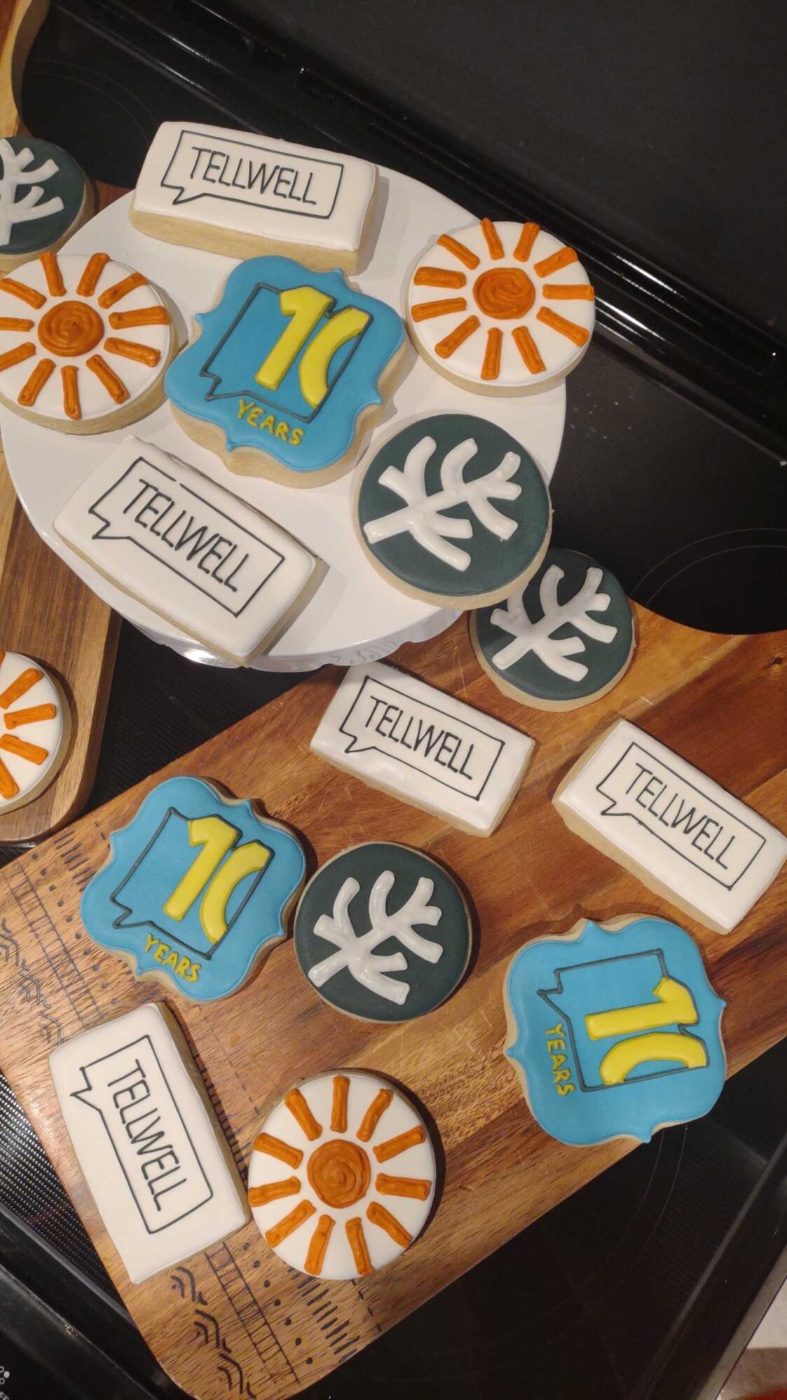 Decorated cookies on trays featuring "Tellwell," sun, and leaf designs, plus a blue cookie with "10 years" in yellow.