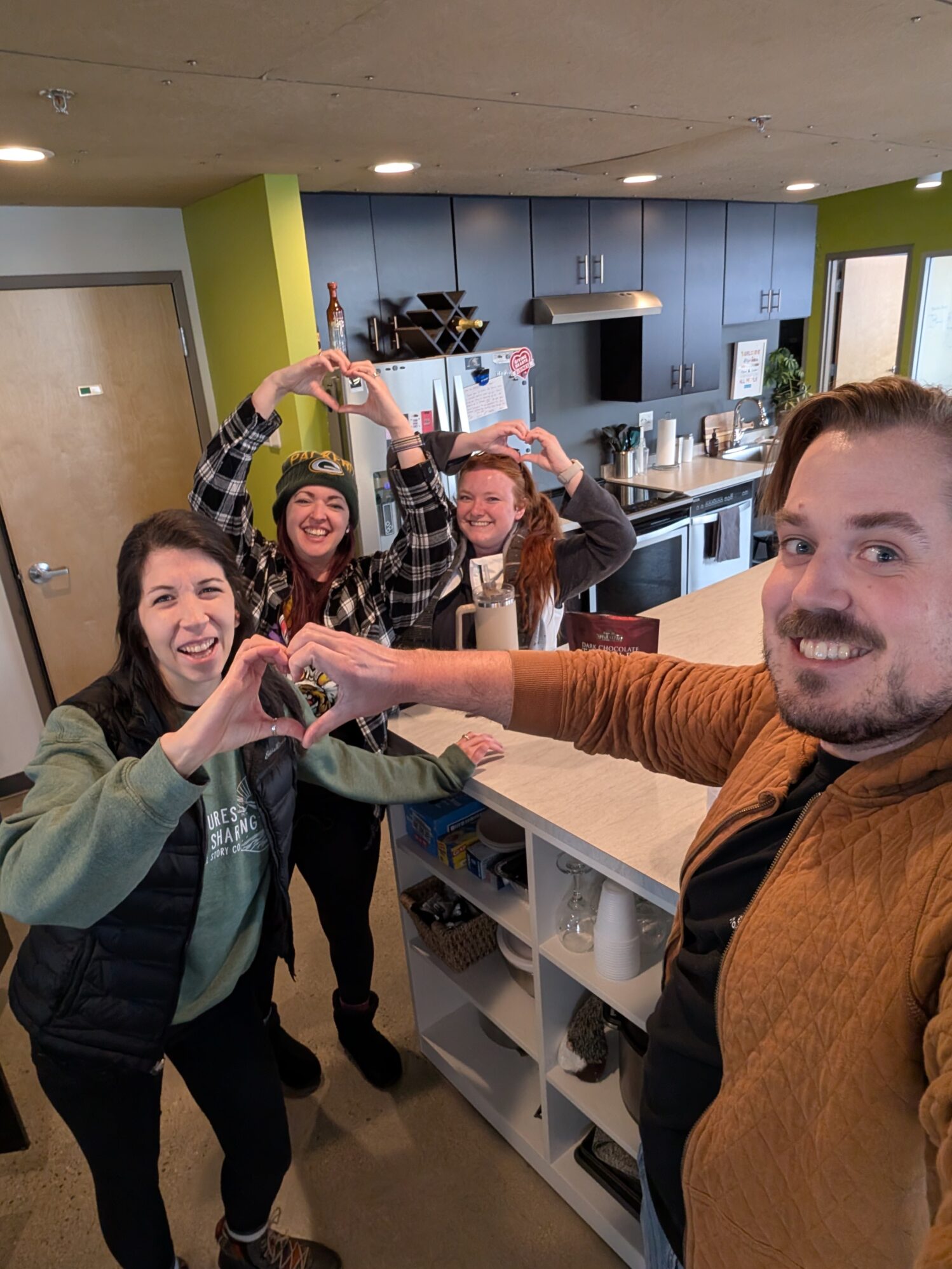 Four individuals make heart shapes with their hands as they smile at the camera.