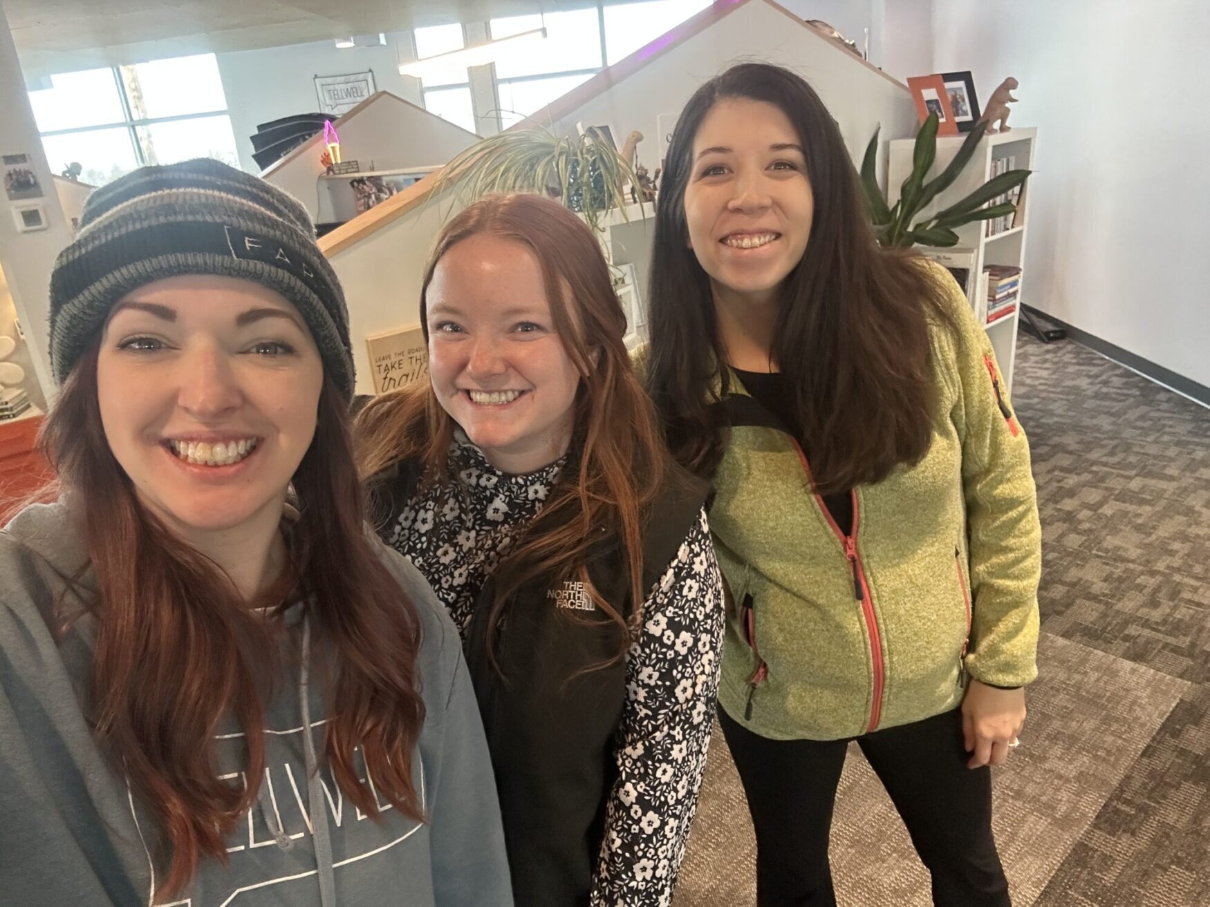 Three women pose for a photo. They are in a warm office setting with friendly smiles.