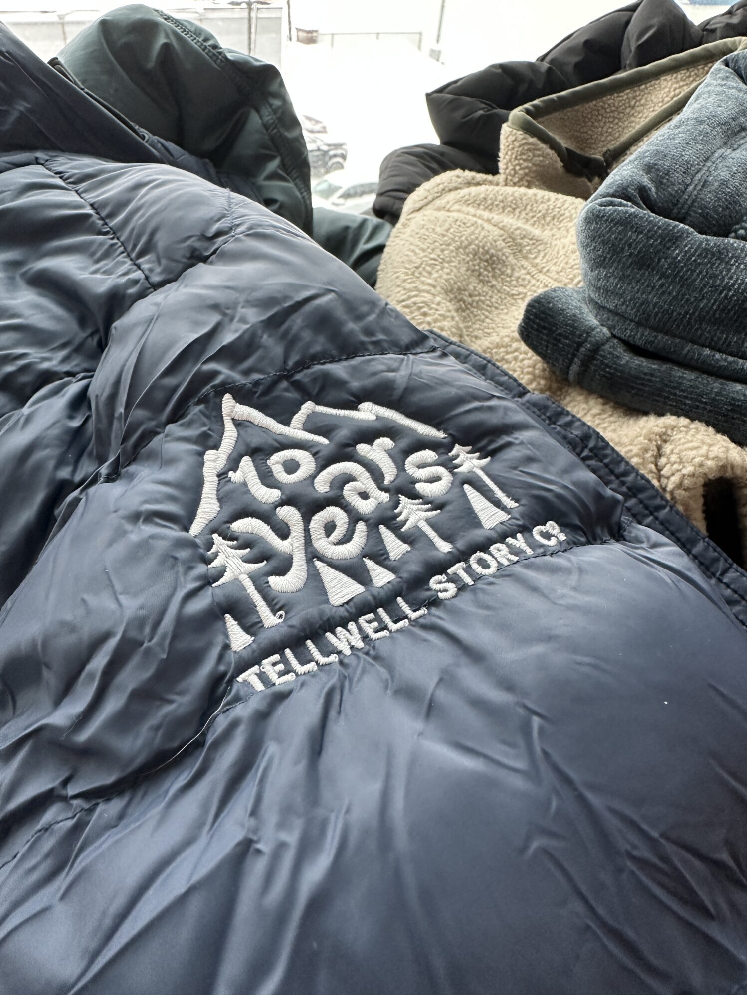 The photo is a close-up shot of a dark blue jacket sleeve with a white embroidered design that reads “10 years Tellwell Story Co.”