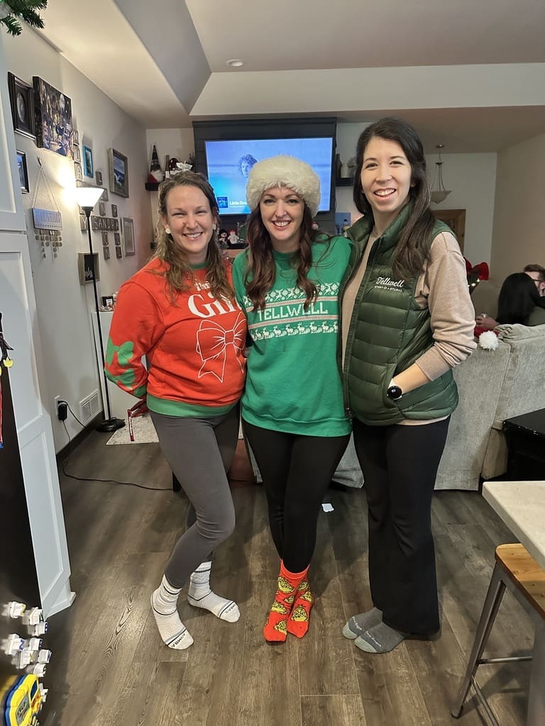 Three women pose for a photo, smiling with festive outfits. The atmosphere is warm and it appears to be a Christmas party.