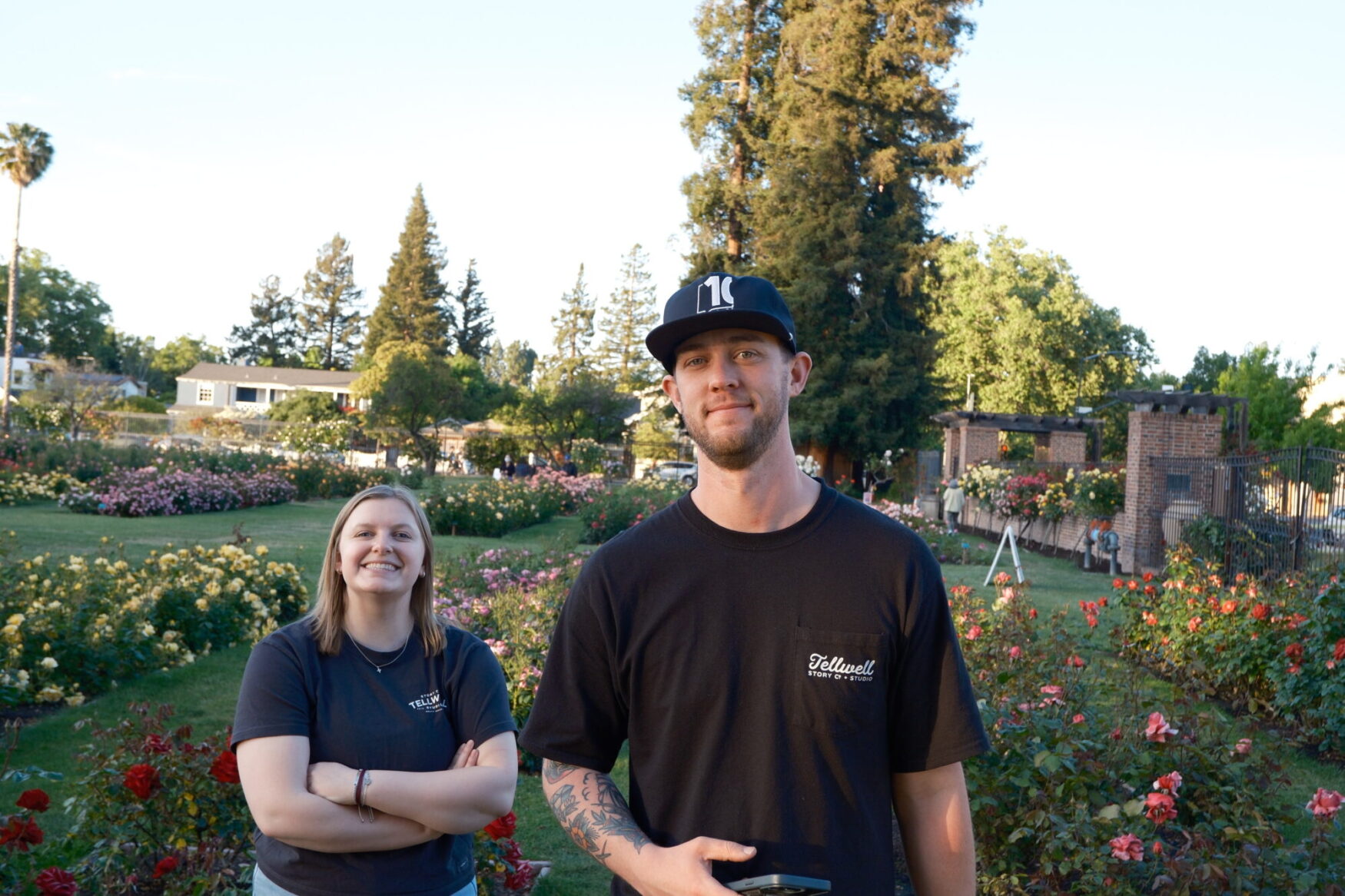 Two individuals stand in a rose garden looking at the camera with a smile.