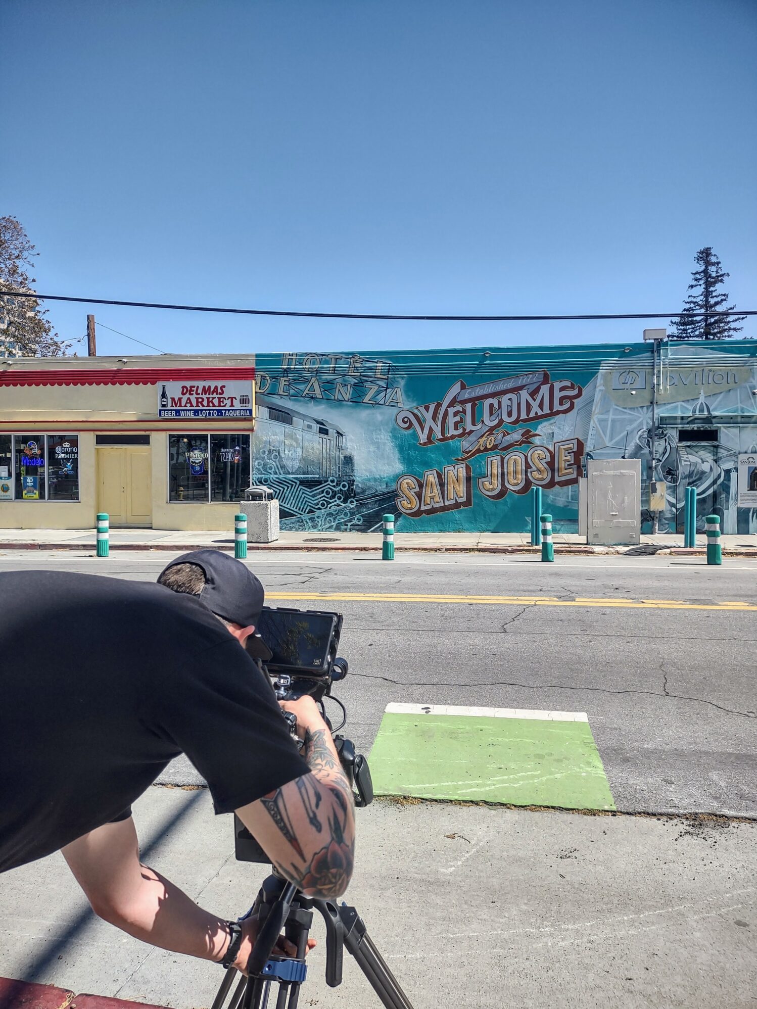 A man films the mural on the side of building that says “welcome to san jose”