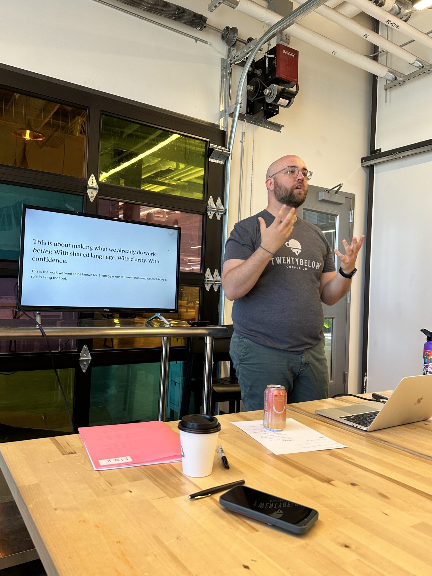 A man wearing a “Twenty Below” shirt standing next to a TV giving a presentation.