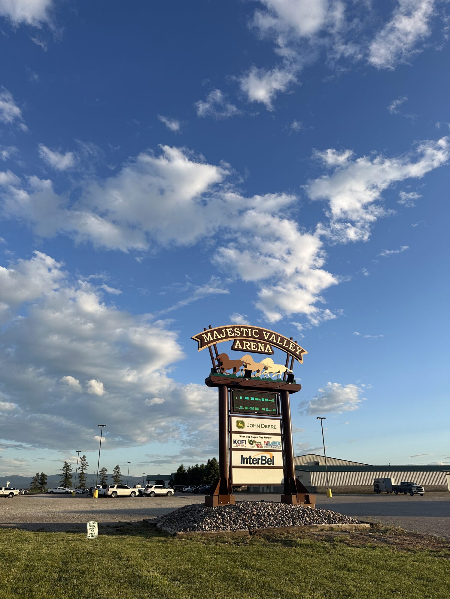 A sign reading "Majestic Valley Arena" standing in a gravel pile. The sky is clear and bright blue with a few clouds.