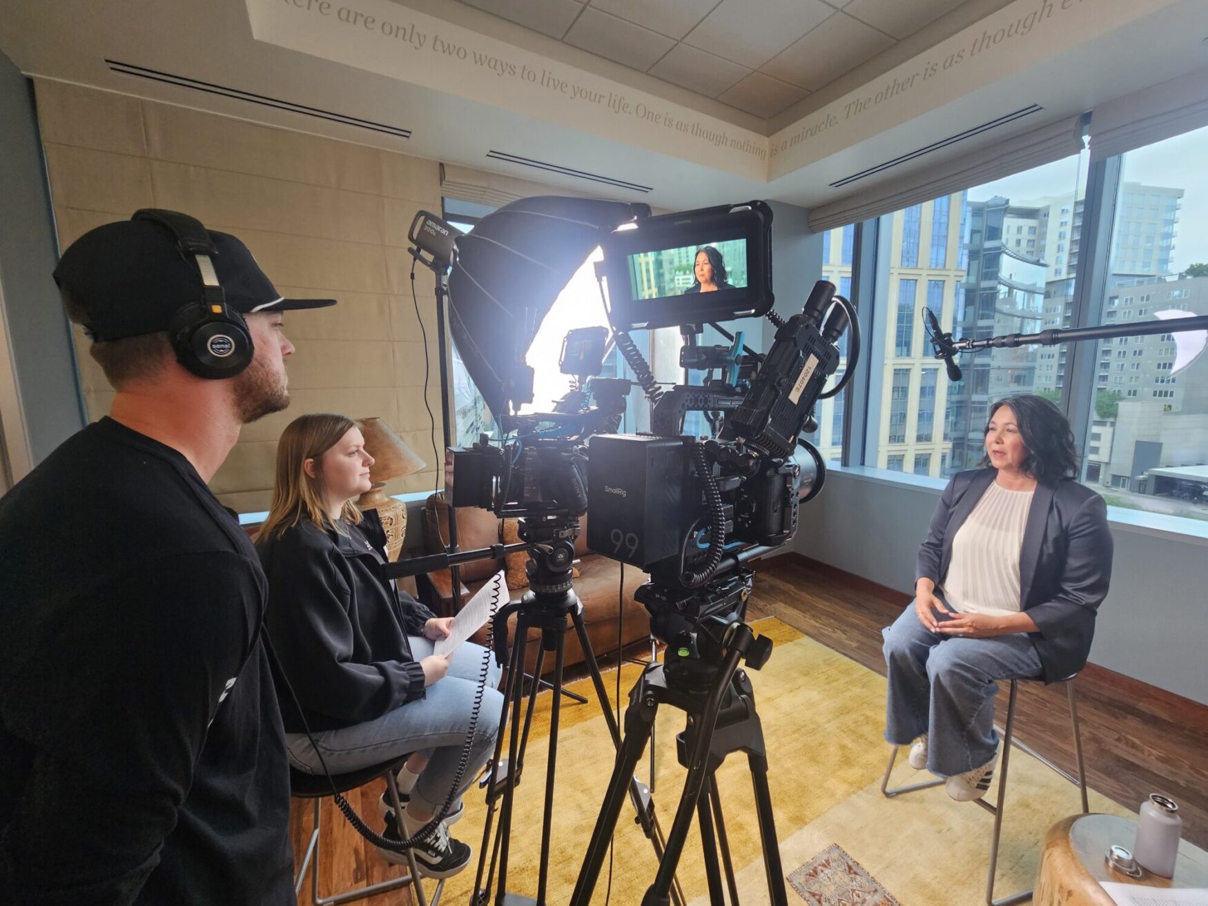 A man is focused on the camera while a woman interviews a female subject, both sitting in a professional setting.