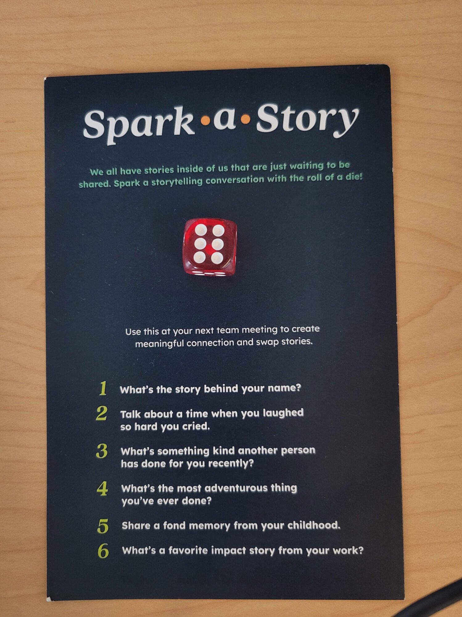 A piece of paper that reads “Spark A Story” at the top. There is a small die attached to the paper, so the participants can play the game that is instructed on the card.