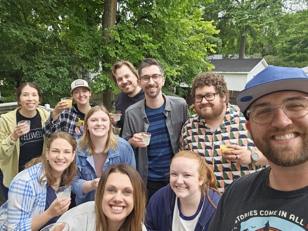 A group poses for a photo, each holding a glass filled with juice. They are outdoors.