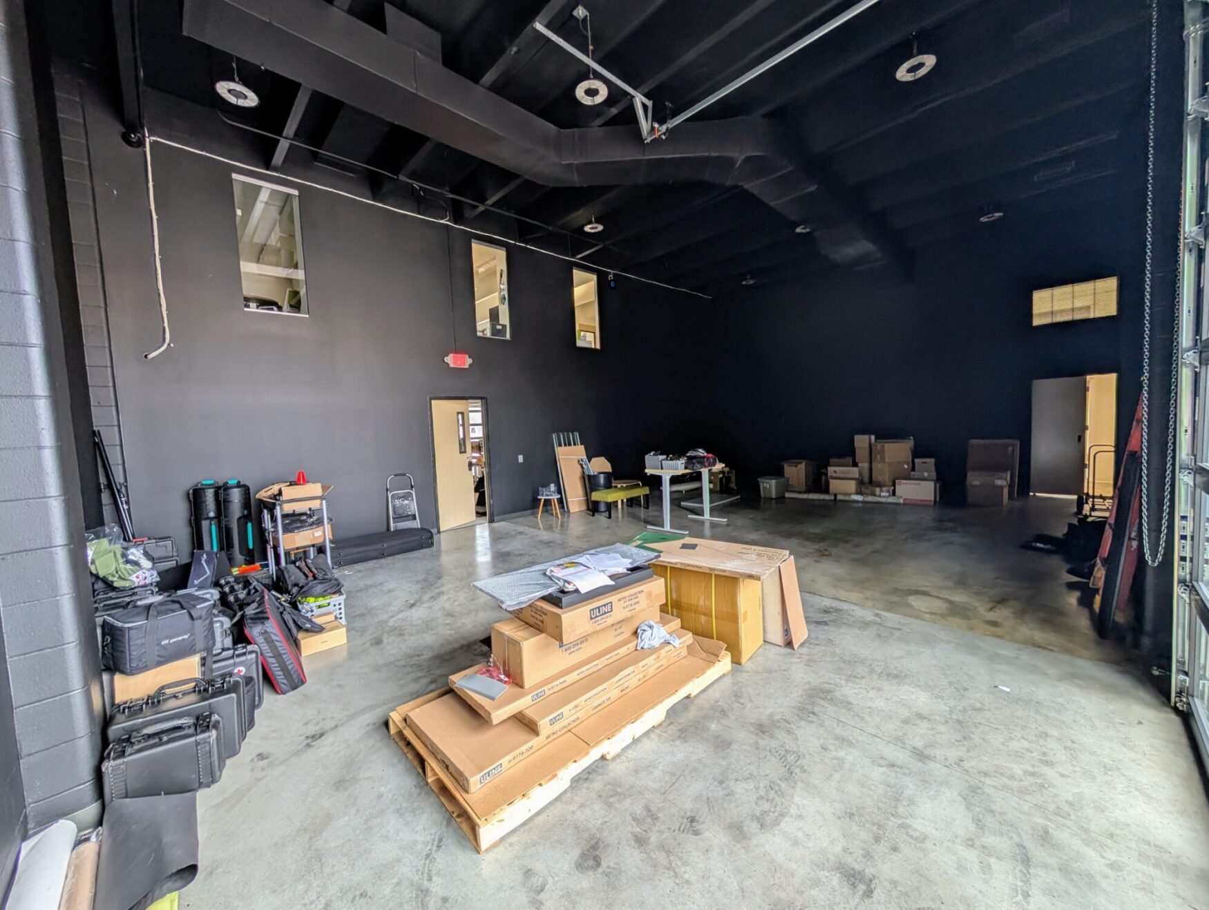 A large room with black walls and ceiling filled with moving materials. This appears to be a film studio in the process of moving in.