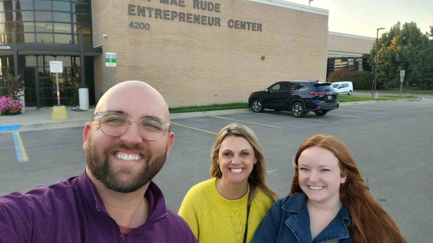 Three Tellwell team members smiling in front of the Mae Rude Entrepreneur Center in Grand Forks on a sunny day.