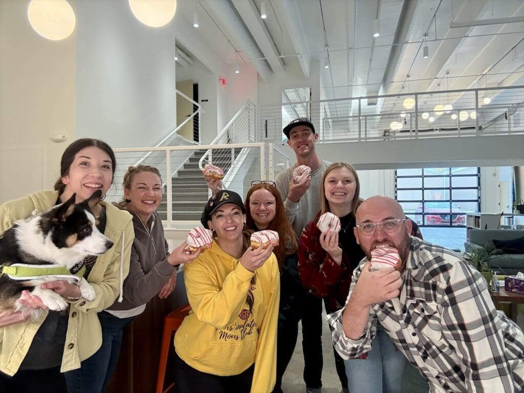 A group of seven people smile for a photo while each holding a donut.