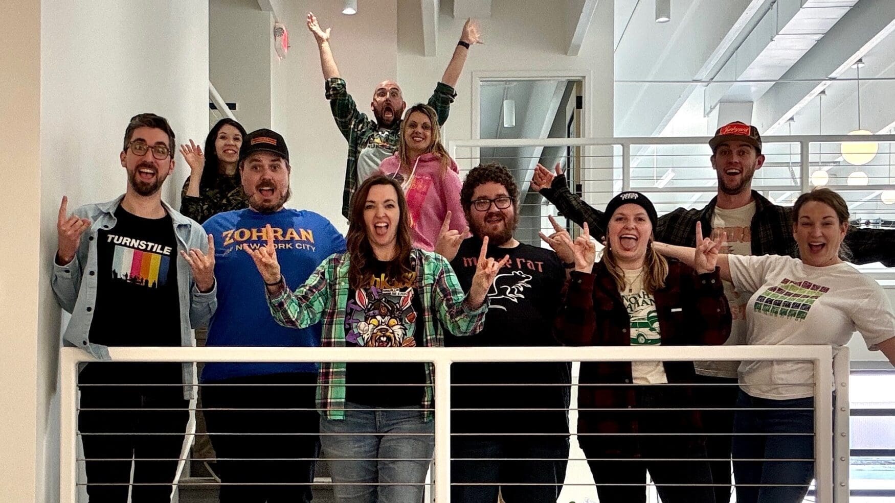 A group of 10 men and women stand on a set of stairs for a photo. They are all smiling or have excited expressions, with several people giving the “rock out” hand symbol.