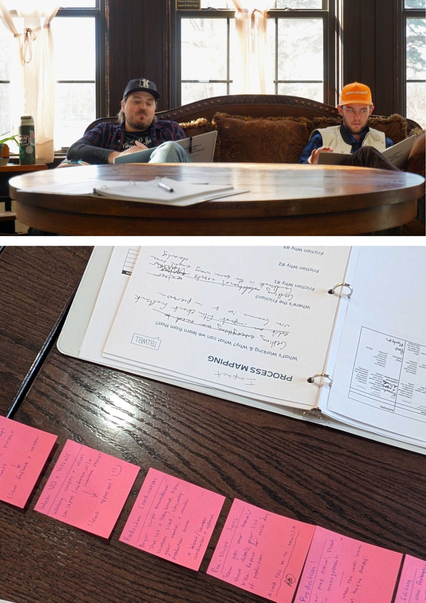 Two people sit at a round table with open notebooks, appearing focused and contemplative. Below, pink sticky notes and a process mapping document are on a wooden table. Bright natural light filters through tall windows, creating a reflective atmosphere.