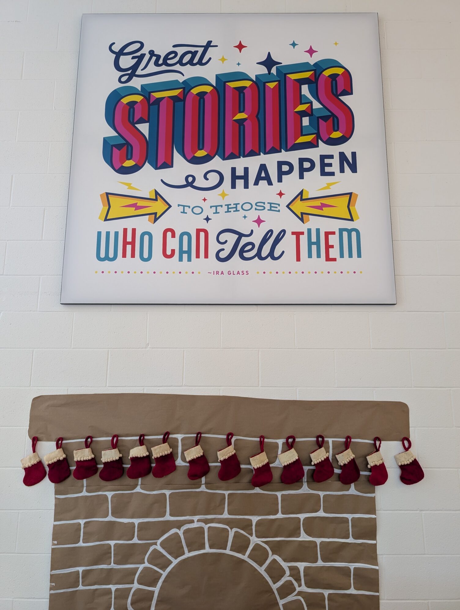 A colorful sign reads, "Great stories happen to those who can tell them." Below is a paper fireplace with small red stockings hanging.