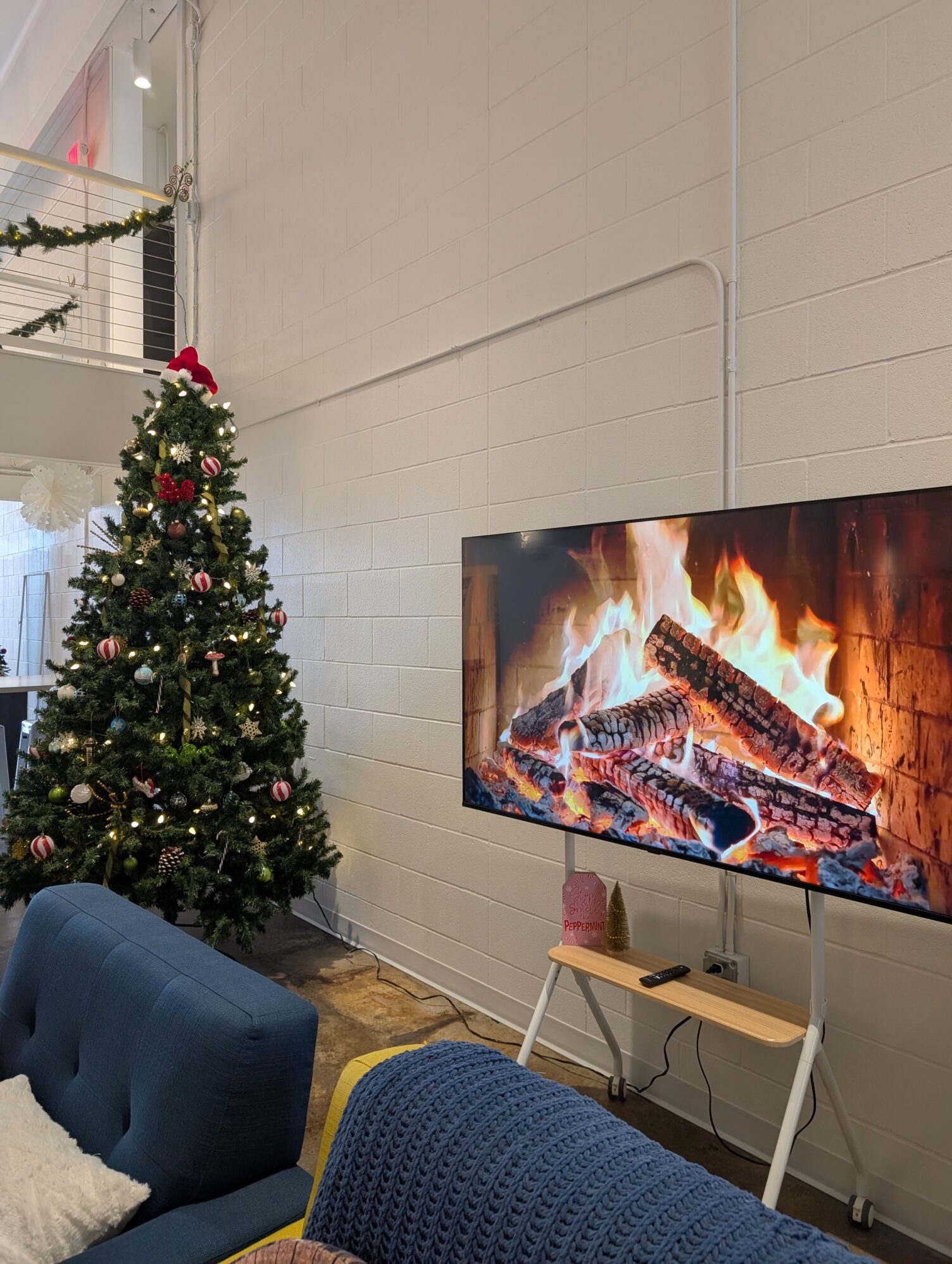 A cozy room features a decorated Christmas tree with red and white ornaments. A TV displays a crackling fireplace, enhancing the festive atmosphere.