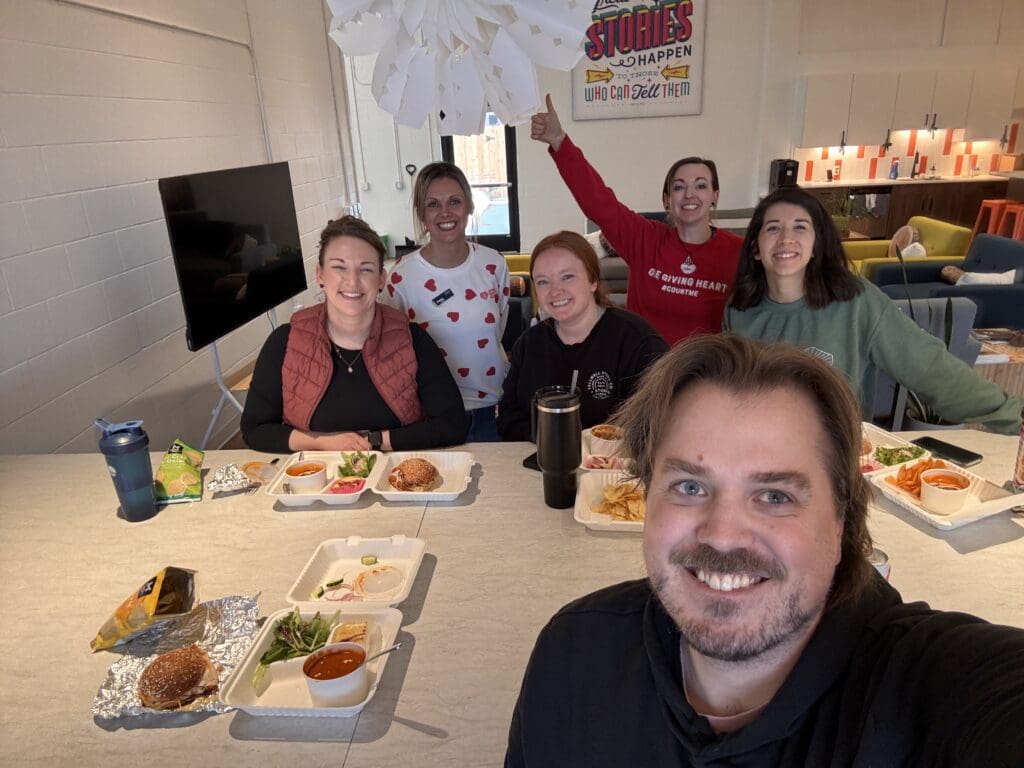 Team of six around a table eating lunch posing.